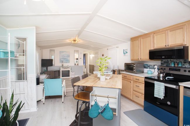 Kitchen featuring stainless steel electric stove, black microwave, light brown cabinetry, lofted ceiling, and light wood-style floors | Image 12