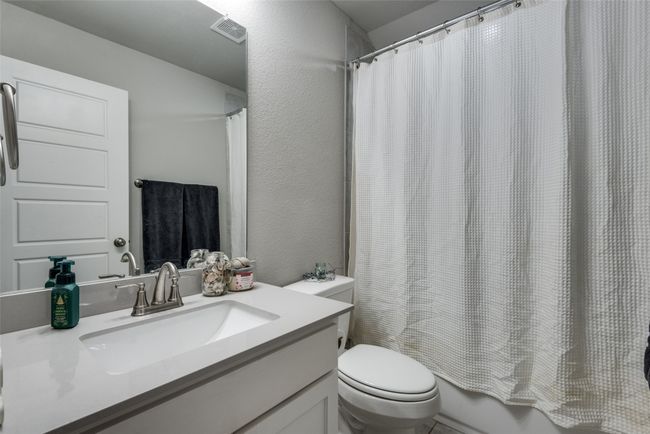 Full bathroom with toilet, visible vents, shower / bath combo with shower curtain, a textured wall, and vanity | Image 23