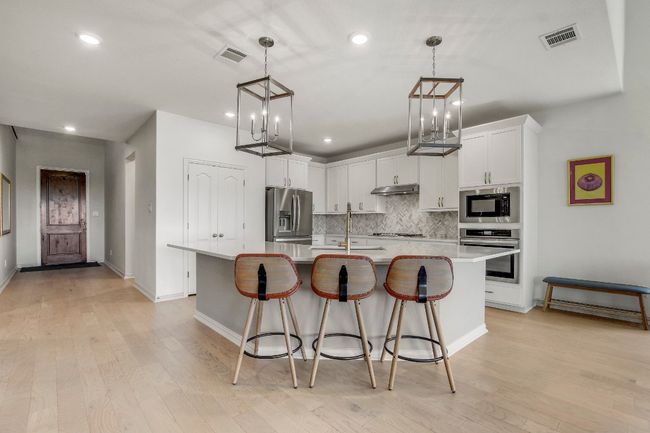 Kitchen featuring stainless steel finishes, custom tile backsplash, recessed lighting, light countertops, and a kitchen island with sink | Image 6