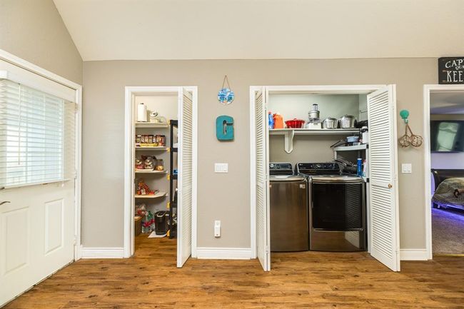 This photo shows utility space with a walk-in pantry on the left and a laundry area on the right, featuring modern appliances. The room has neutral flooring and neutral walls, providing a clean and organized look. | Image 12