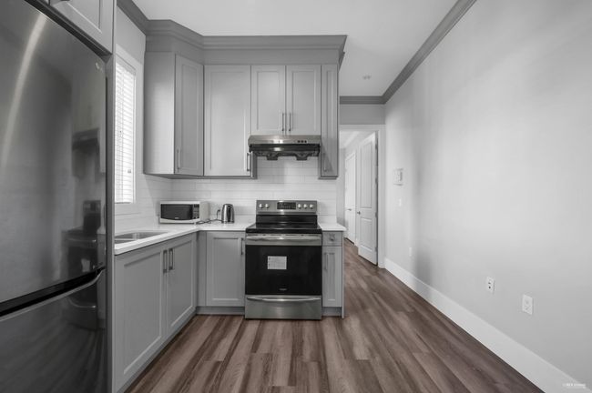 Kitchen with stainless steel appliances, gray cabinetry, range hood, light countertops, and decorative backsplash | Image 22