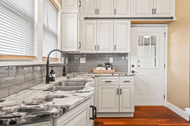 kitchen with light stone countertops, decorative backsplash, white cabinets, and dark wood-style floors | Image 18