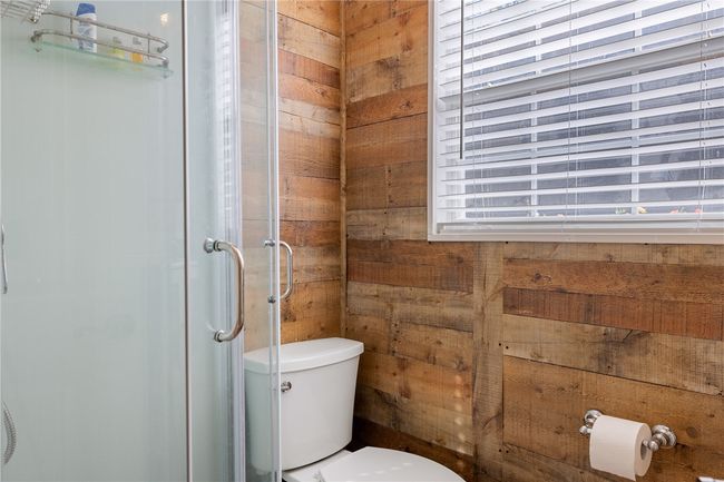 Full bathroom featuring a shower stall, wooden walls, and toilet | Image 16