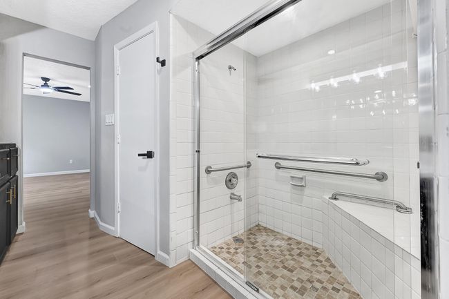 The primary bathroom offers a spacious walk-in shower with clean white tile, a built-in bench, and multiple grab bars—designed for both comfort and accessibility. | Image 30