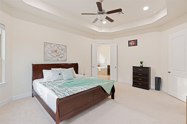 Bedroom featuring light colored carpet, a raised ceiling, recessed lighting, ensuite bathroom, and ceiling fan | Image 20