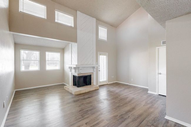 Unfurnished living room with visible vents, a tiled fireplace, wood finished floors, a high ceiling, and baseboards | Image 10