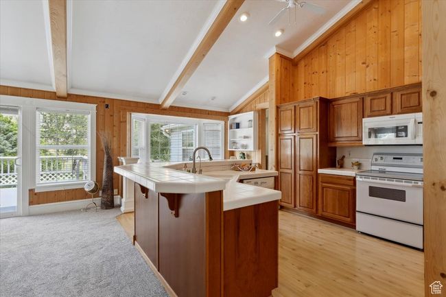 Kitchen with white appliances, tile countertops, wooden walls, a sink, and brown cabinetry | Image 10