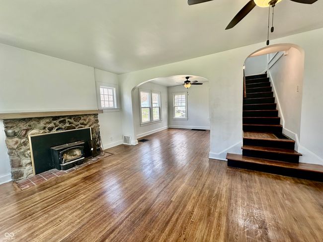 unfurnished living room with ceiling fan, arched walkways, stairway, wood finished floors, and baseboards | Image 20