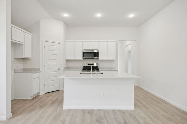 Kitchen featuring an island with sink, appliances with stainless steel finishes, light countertops, light wood finished floors, and white cabinets | Image 6