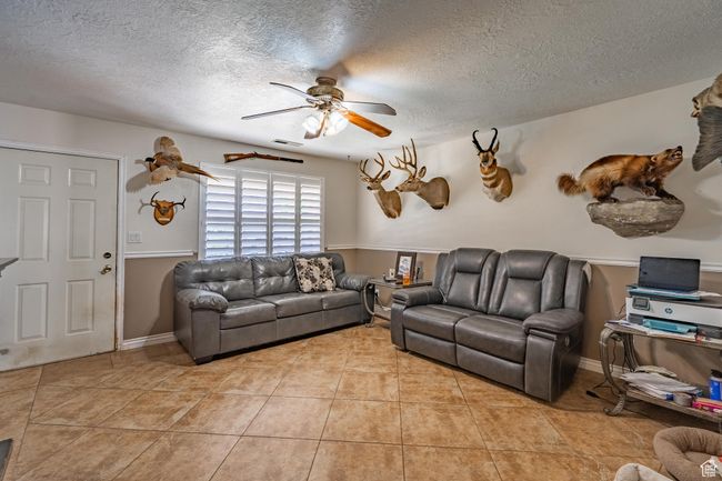 Living room with a ceiling fan, a textured ceiling, and light tile patterned floors | Image 16