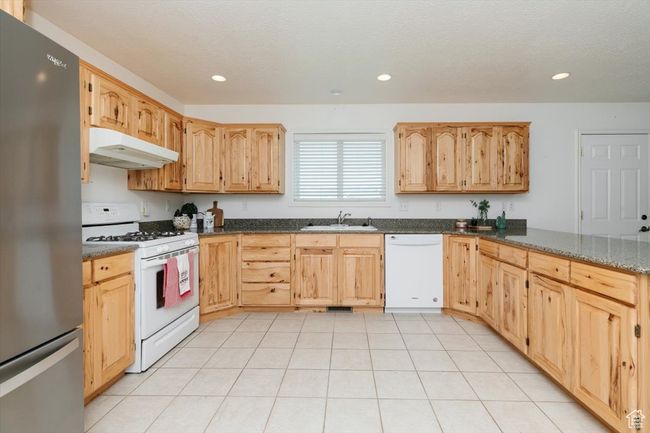 Kitchen featuring white appliances, under cabinet range hood, recessed lighting, dark stone countertops, and light brown cabinets | Image 38