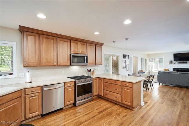 Kitchen with appliances with stainless steel finishes, a peninsula, tasteful backsplash, light wood-style flooring, and recessed lighting | Image 13
