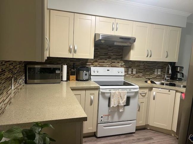 Kitchen with ornamental molding, white electric range, stainless steel microwave, under cabinet range hood, and backsplash | Image 5