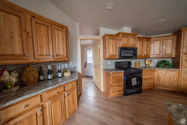 Kitchen with brown cabinets, decorative backsplash, black appliances, light wood-style flooring, and a textured ceiling | Image 28