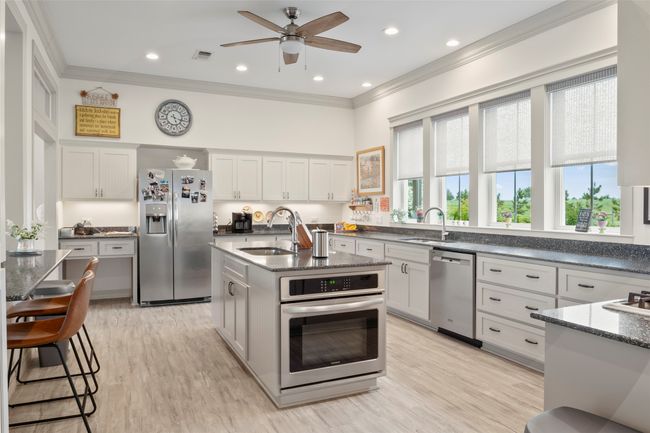 Kitchen featuring a center island with sink, appliances with stainless steel finishes, crown molding, white cabinetry, and a sink | Image 13