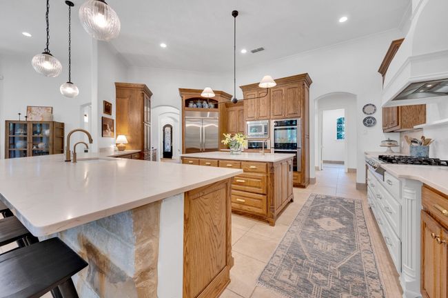 Kitchen featuring a sink, built in appliances, custom range hood, arched walkways, and an island with sink | Image 15