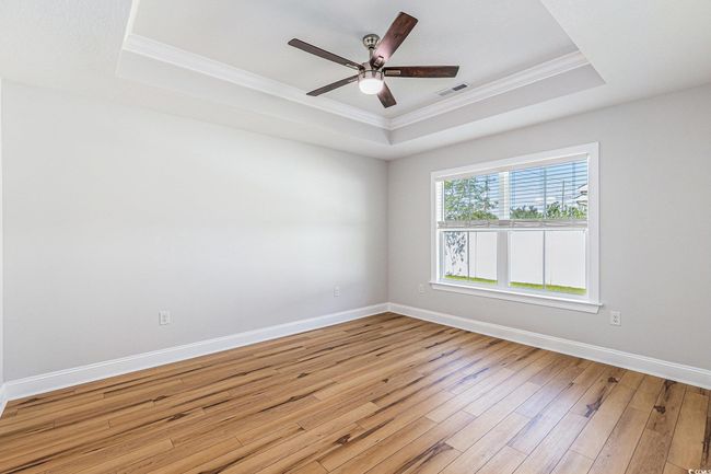 Spare room with a tray ceiling, crown molding, wood finished floors, and a ceiling fan | Image 14