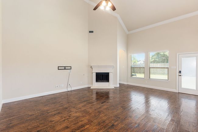 Unfurnished living room featuring a fireplace with raised hearth, a ceiling fan, high vaulted ceiling, dark wood-type flooring, and ornamental molding | Image 15
