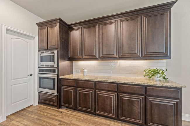 Kitchen featuring light wood-style flooring, stainless steel appliances, dark brown cabinetry, and light stone countertops | Image 10