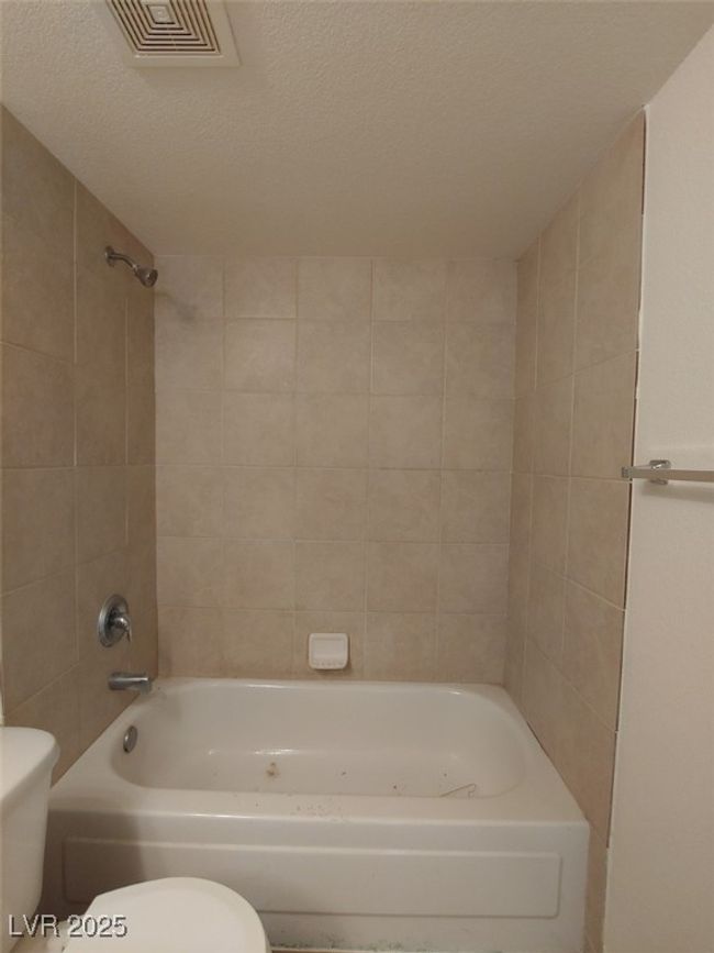 Bathroom with tiled shower / bath combo, a textured ceiling, and toilet | Image 12