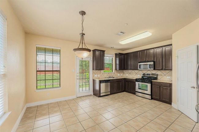 Kitchen with stainless steel appliances, tasteful backsplash, light countertops, and dark brown cabinetry | Image 7