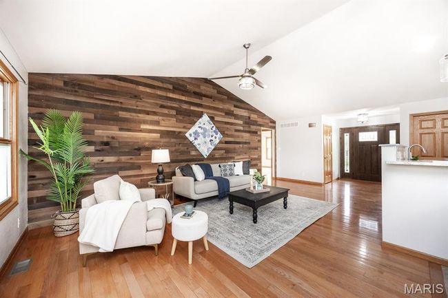 Living room featuring wooden walls, a ceiling fan, hardwood / wood-style floors, baseboards, and healthy amount of natural light | Image 11