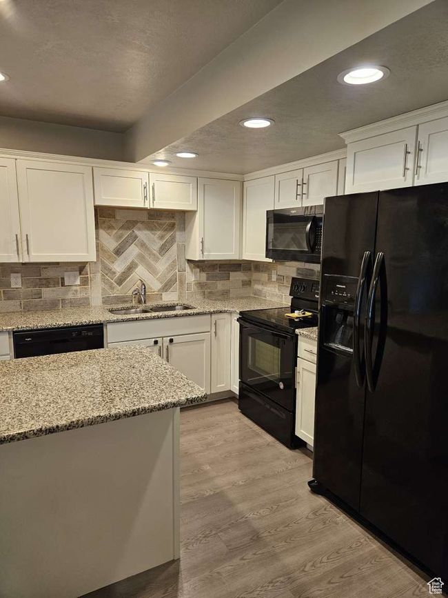 Kitchen featuring white cabinets, light wood-style floors, a sink, and black appliances | Image 6