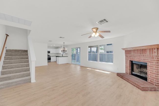 Unfurnished living room with a fireplace, light wood-type flooring, visible vents, and ceiling fan with notable chandelier | Image 5