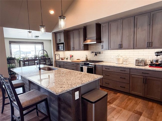 Kitchen featuring a breakfast bar area, a sink, wood finished floors, appliances with stainless steel finishes, and wall chimney range hood | Image 6