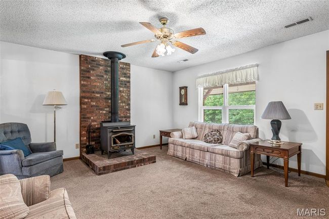 Carpeted living room with a wood stove, a ceiling fan, a textured ceiling, and baseboards | Image 12