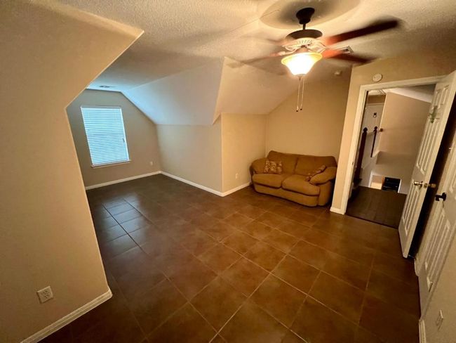 Additional living space featuring dark tile patterned flooring, a textured ceiling, vaulted ceiling, and ceiling fan | Image 12