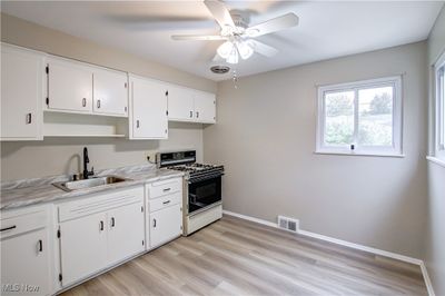 Kitchen with ceiling fan, white cabinets, sink, white range with gas stovetop, and light wood-type flooring | Image 2