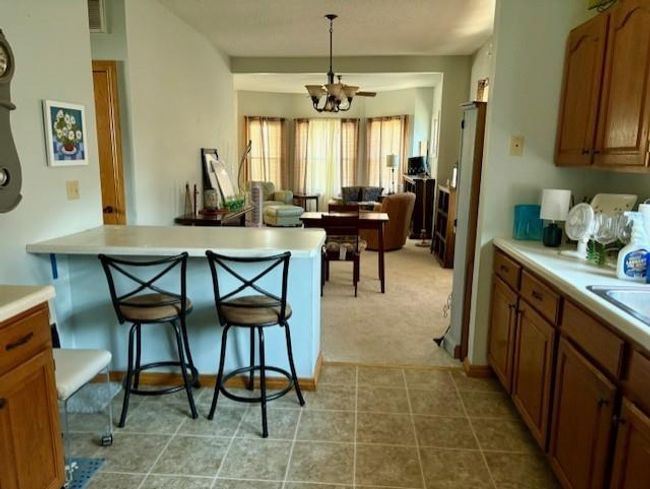 Kitchen featuring light countertops, a breakfast bar area, a chandelier, visible vents, and brown cabinetry | Image 14