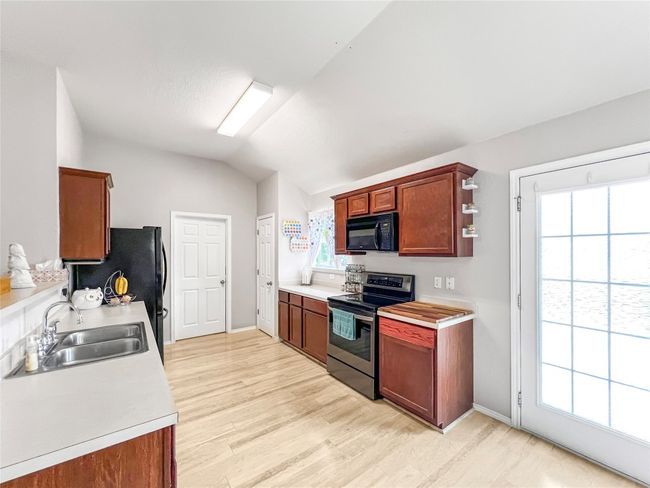 Kitchen featuring black appliances, a sink, light countertops, vaulted ceiling, and light wood-style floors | Image 12