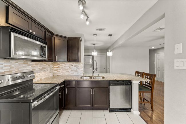 Kitchen featuring stainless steel appliances, a peninsula, dark brown cabinets, decorative backsplash, and light stone countertops | Image 18
