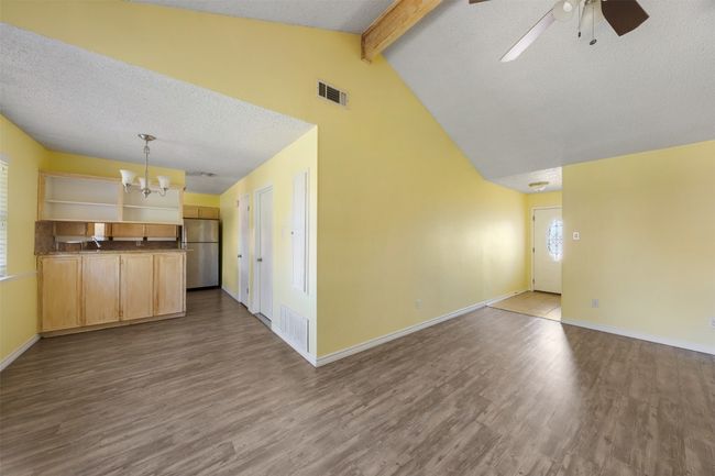 Unfurnished living room with a textured ceiling, beamed ceiling, a chandelier, wood finished floors, and a ceiling fan | Image 9