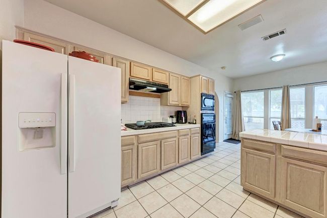 Kitchen featuring black appliances, under cabinet range hood, light brown cabinetry, tasteful backsplash, and light tile patterned floors | Image 18