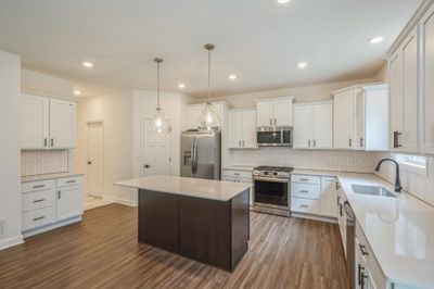 (Photo of a decorated model, actual homes finishes will vary) This stunning kitchen features a large center island, quartz countertops, LVP floors, stainless appliances and more! | Image 3