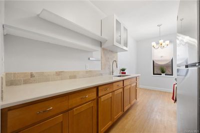 Kitchen featuring hanging light fixtures, sink, backsplash, light hardwood / wood-style flooring, and an inviting chandelier | Image 3