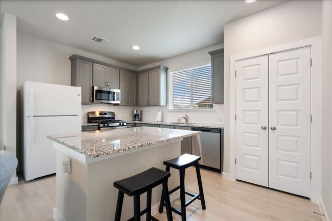Kitchen featuring stainless steel appliances, a kitchen island, light wood-style floors, light stone countertops, and a breakfast bar | Image 9