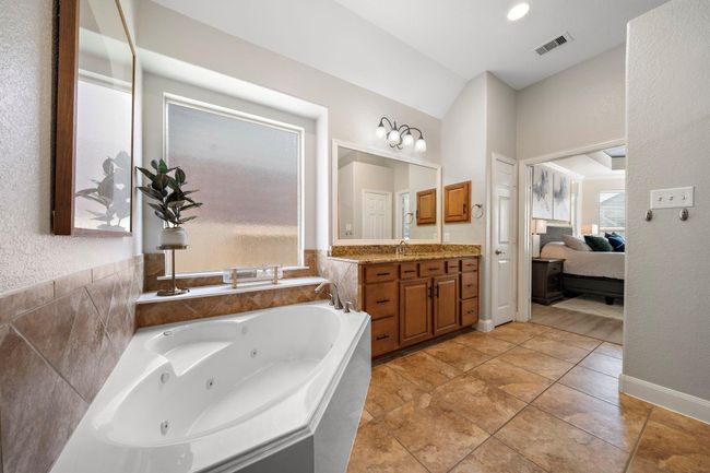 Indulge in the spa-like serenity of the primary bath, complete with a luxurious soaking tub and dual vanities featuring granite countertops. The glass-enclosed shower enhances the space's elegance, while warm tile flooring and natural light create an inviting atmosphere for relaxation and rejuvenation. | Image 32