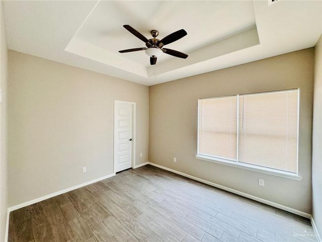 Empty room with a raised ceiling, a ceiling fan, and wood finished floors | Image 5