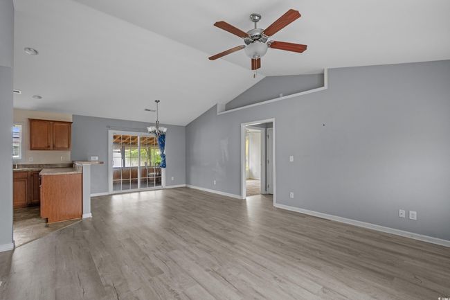 Unfurnished living room with a chandelier, ceiling fan, lofted ceiling, baseboards, and light wood-style floors | Image 13