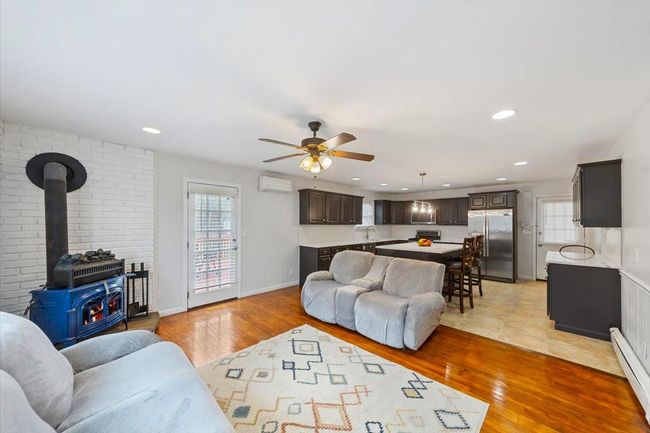 Living room with a wall mounted air conditioner, ceiling fan, light wood-type flooring, and baseboard heating | Image 38
