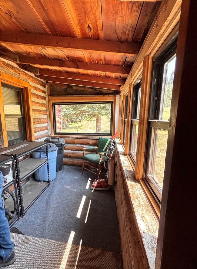 Unfurnished sunroom with a wood ceiling with exposed beams, rustic walls, and carpet flooring | Image 22