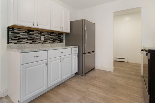 Kitchen featuring a baseboard heating unit, stove, white cabinets, backsplash, and freestanding refrigerator | Image 14