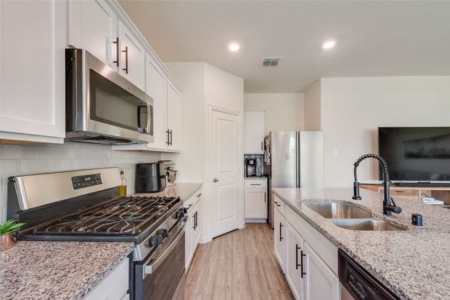 Kitchen with appliances with stainless steel finishes, white cabinets, light wood-type flooring, tasteful backsplash, and light stone countertops | Image 6
