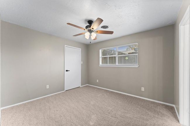 Master bedroom with neutral walls and carpet, featuring a ceiling fan with lights. Window allows for ample natural light. | Image 25