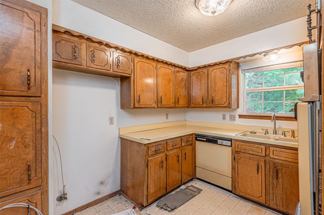 Kitchen featuring refrigerator, brown cabinets, a sink, a textured ceiling, and dishwashing machine | Image 25