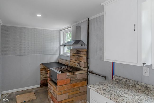 detailed view of wall chimney exhaust hood, ornamental molding, white cabinets, baseboards, and light stone counters | Image 47